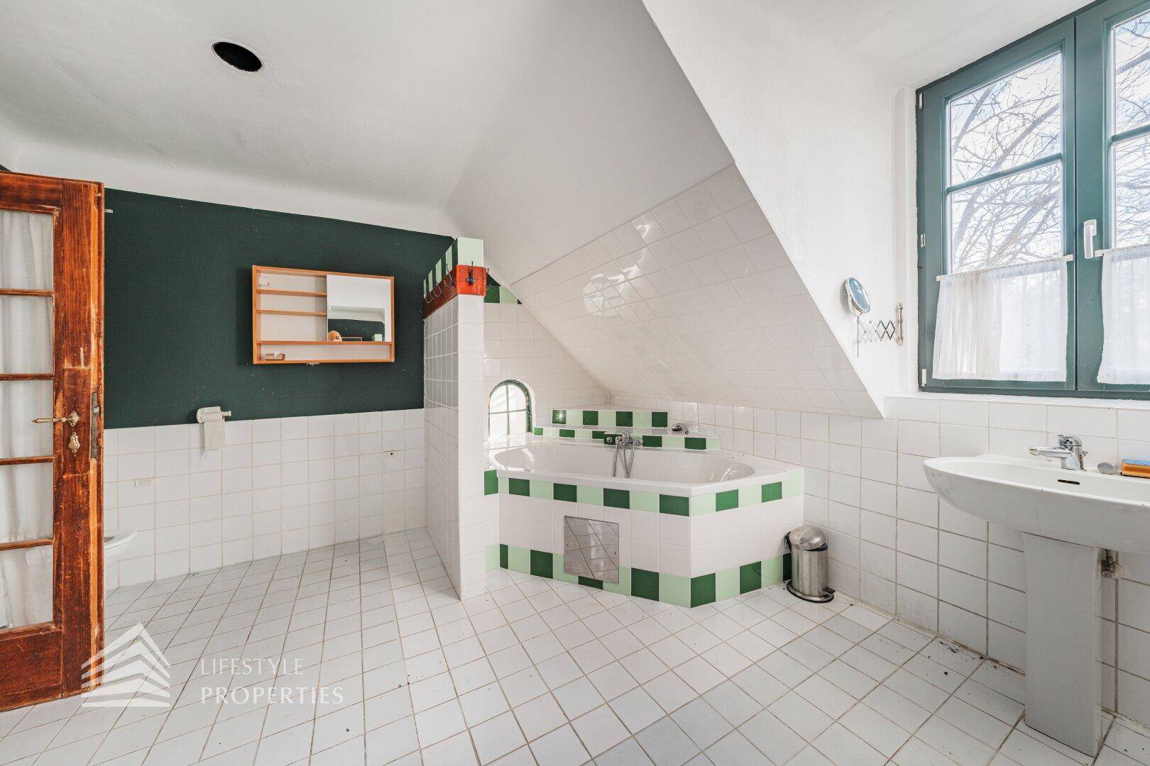 Geräumiges Badezimmer im Dachgeschoss mit Badewanne, weißen Fliesen und grünen Akzenten.