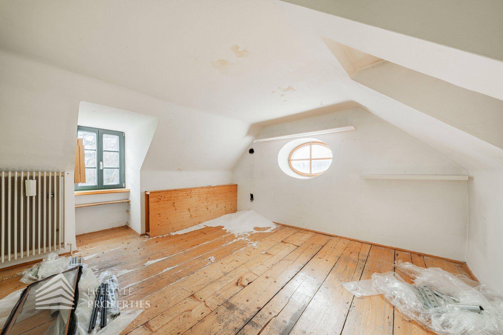 Helles Schlafzimmer im Dachgeschoss mit Holzdielenboden, Dachschrägen und ovalem Fenster.