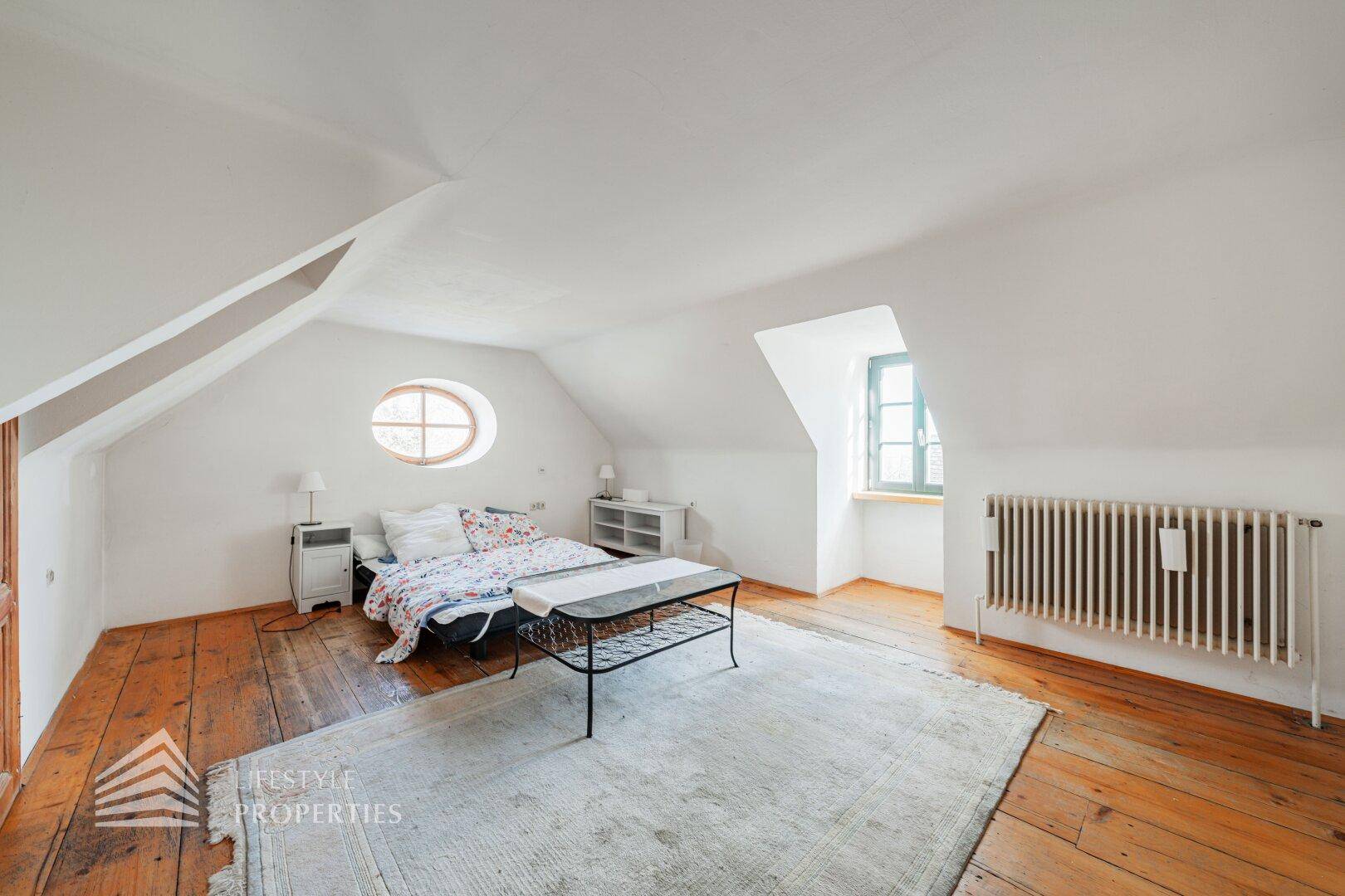 Gemütliches Schlafzimmer im Dachgeschoss mit Holzdielenboden, Dachschrägen und Bett.