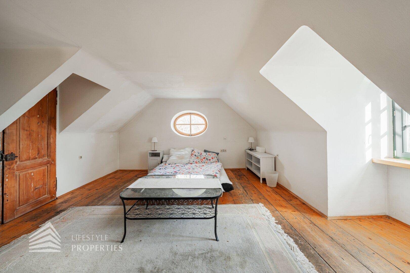 Schlafzimmer im Dachgeschoss mit Holzdielenboden, Dachschrägen und ovalem Fenster.