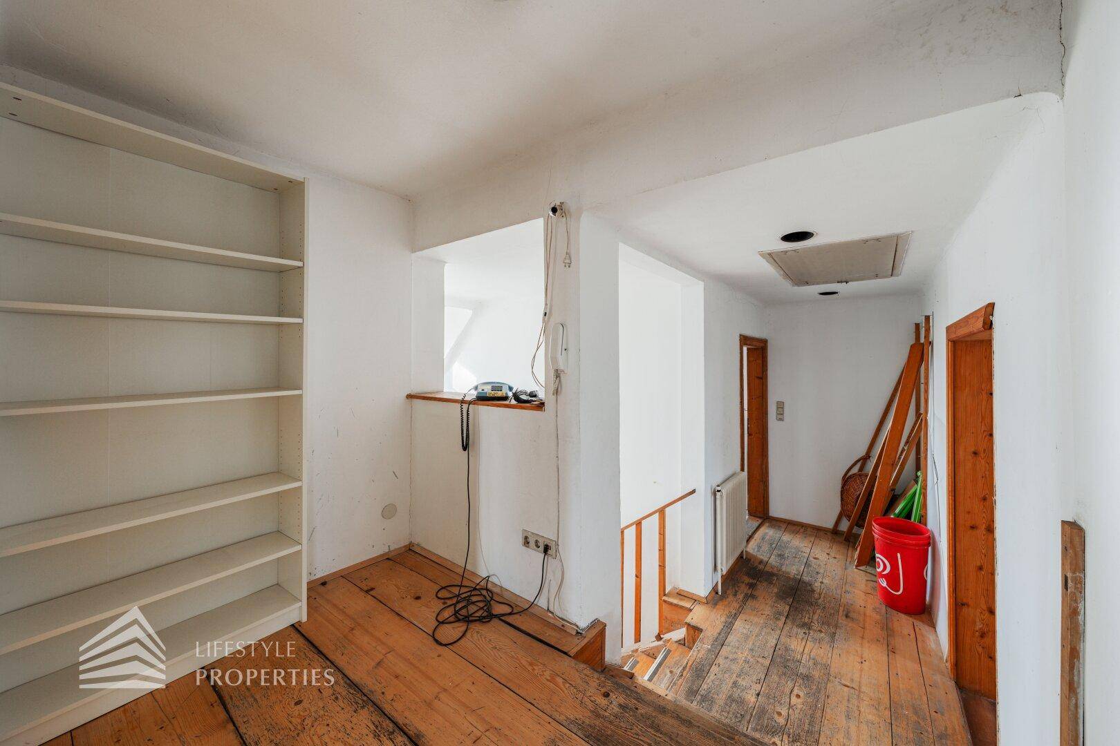 Heller Flur im Dachgeschoss mit Holzdielenboden und eingebautem Regal.