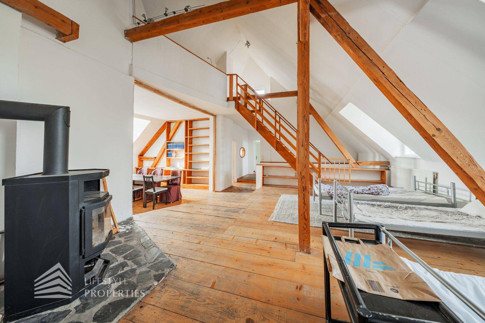 Offener Wohn- und Essbereich im Dachgeschoss mit Holzdielenboden, Holztreppe und Regalen.