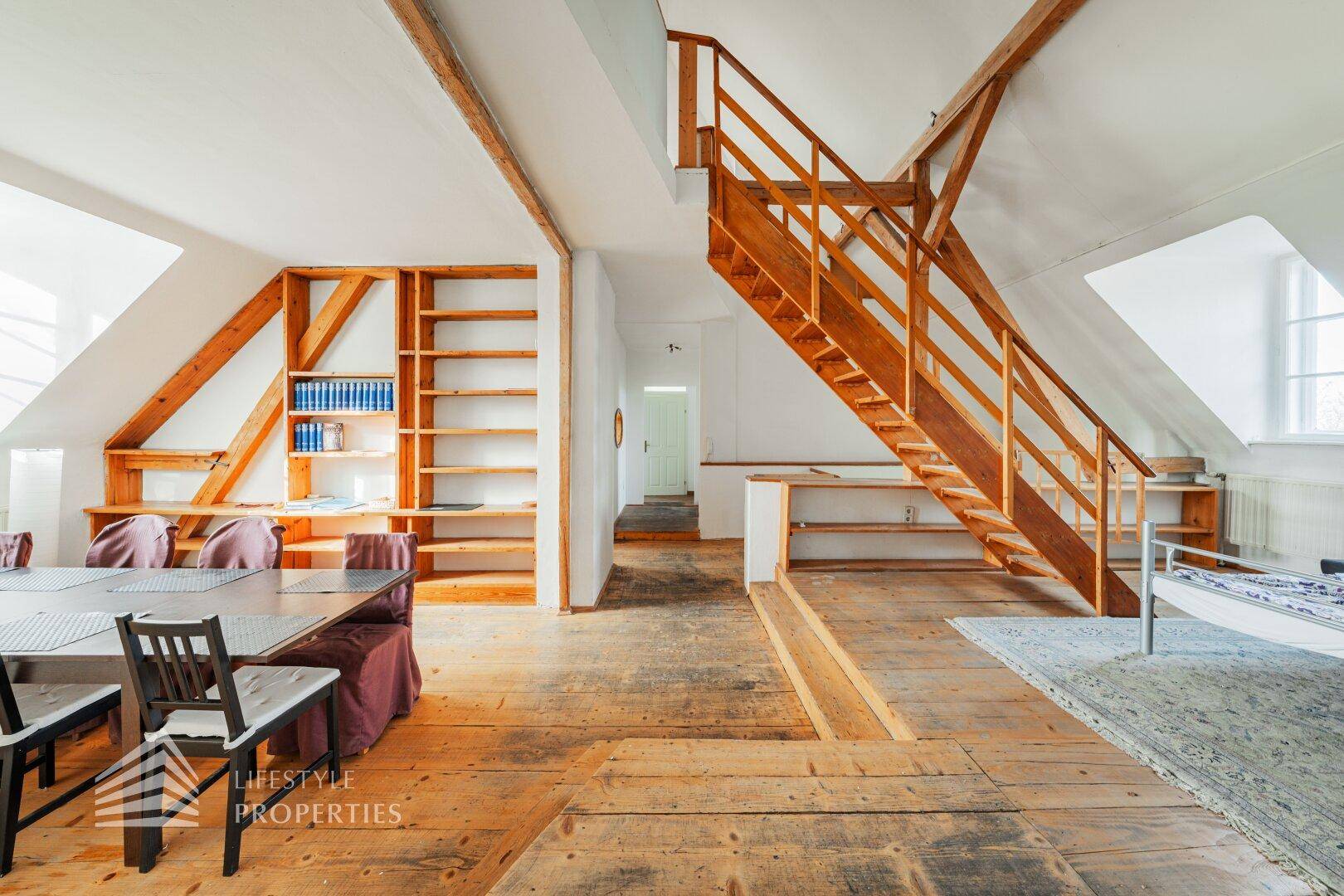Essbereich im Dachgeschoss mit Holzdielenboden, großem Esstisch und eingebauten Regalen.