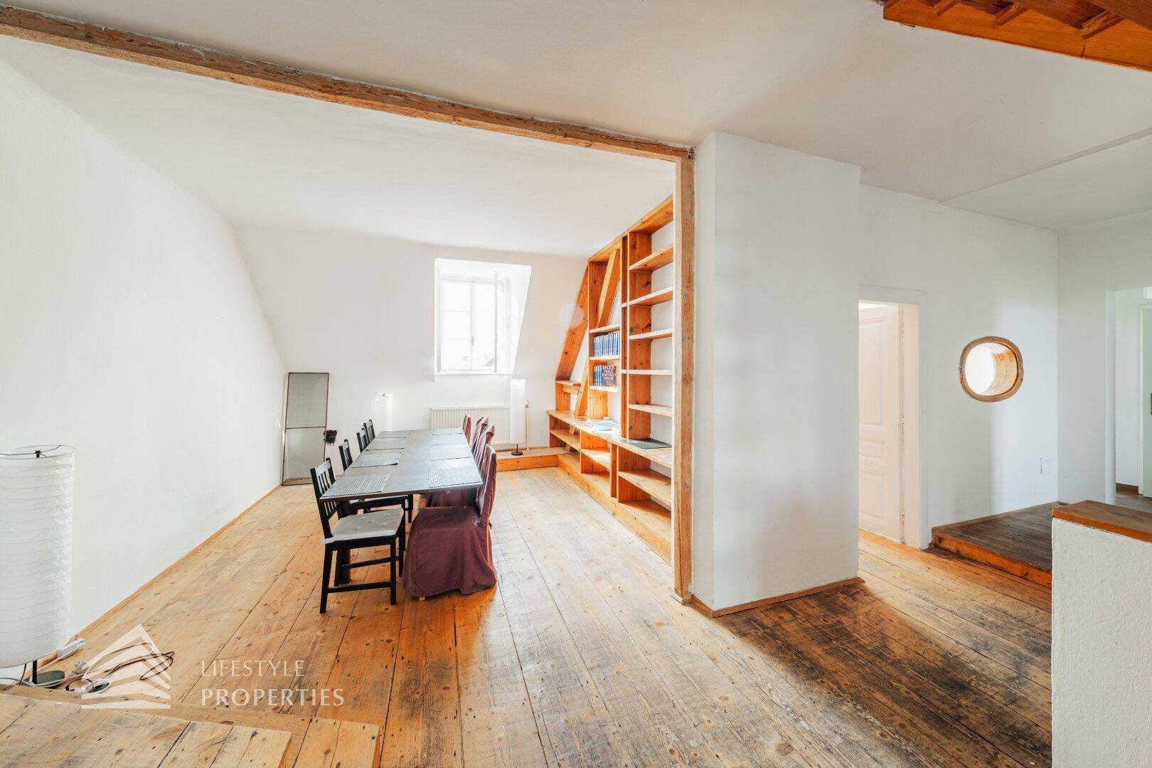 Essbereich im Dachgeschoss mit Holzdielenboden, großem Esstisch und eingebauten Regalen.
