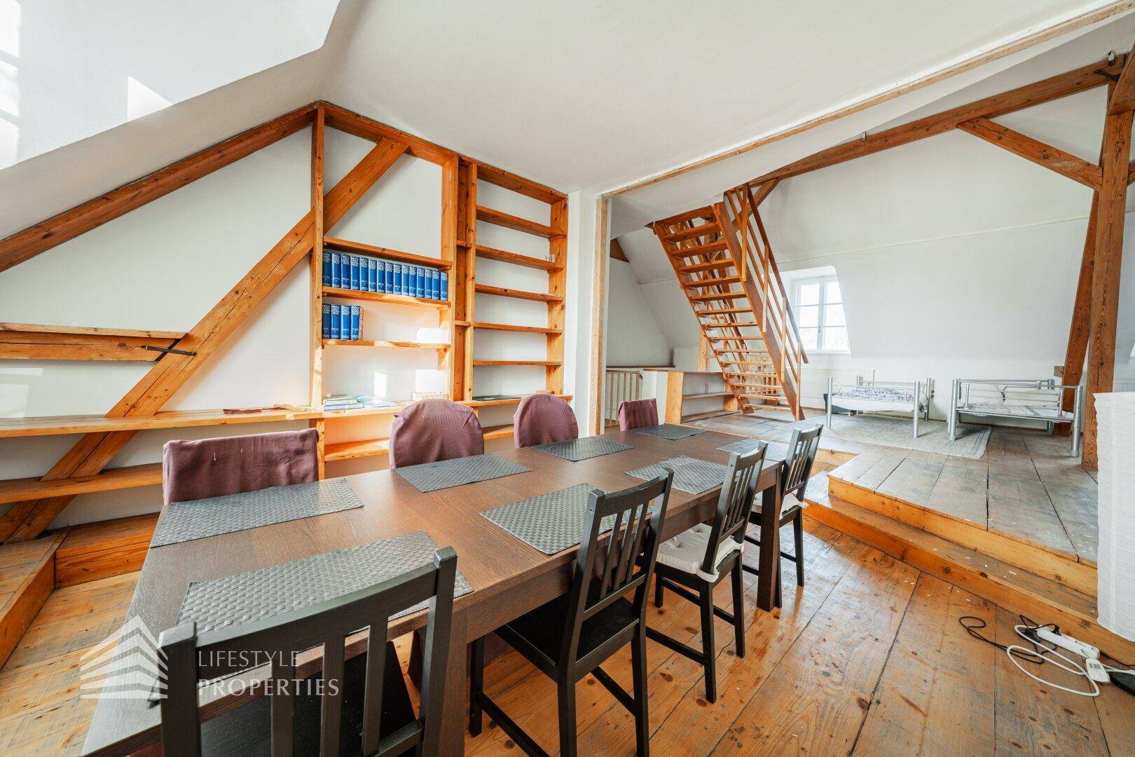 Offener Wohn- und Essbereich im Dachgeschoss mit Holzdielenboden, Kamin und Holztreppe.