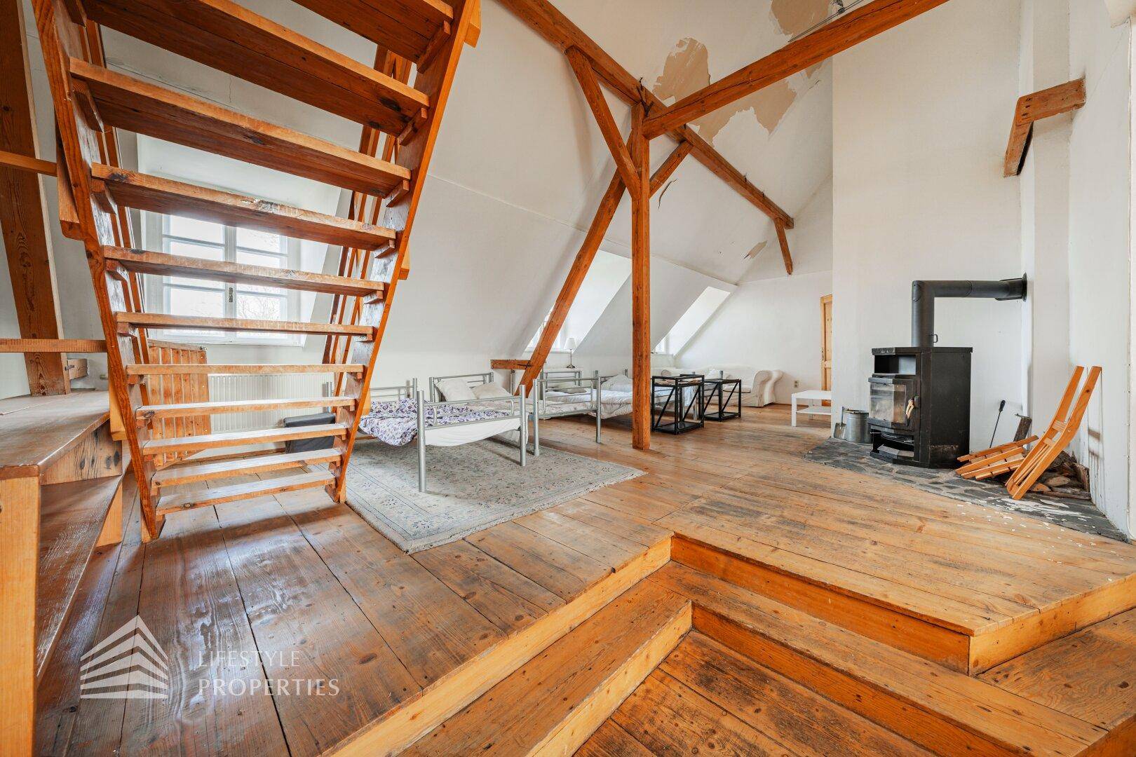 Offener Wohn- und Essbereich im Dachgeschoss mit Holzdielenboden, Kamin und Holztreppe.