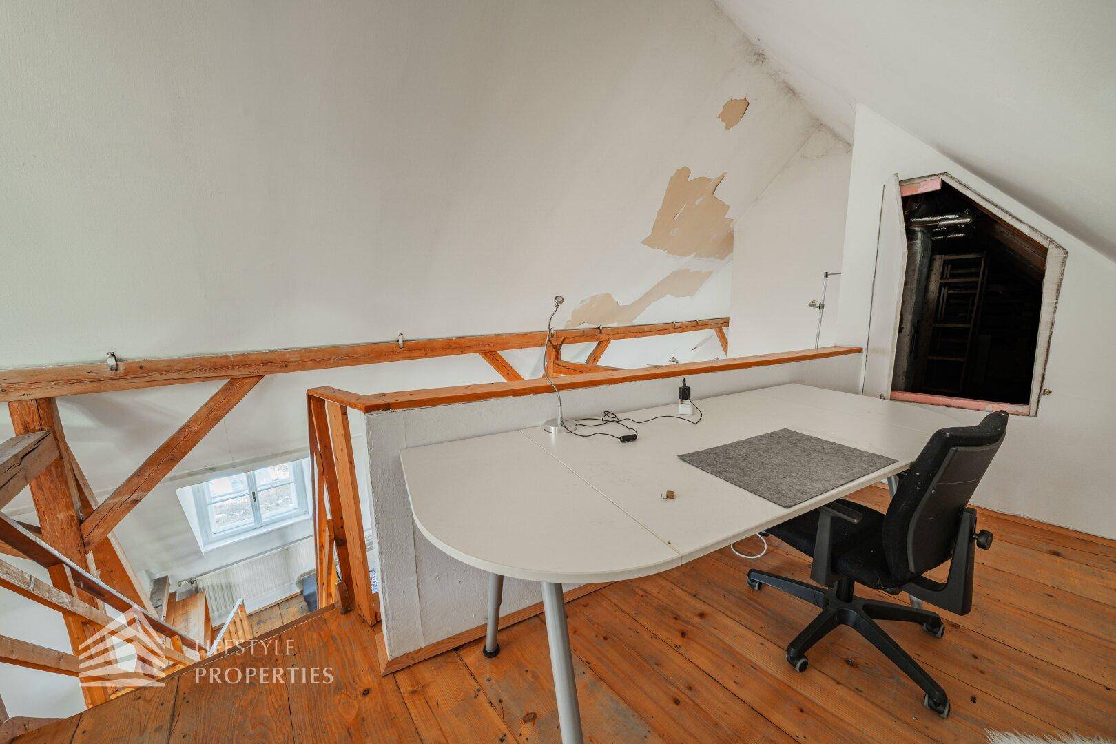 Offener Raum im Dachgeschoss mit Holzdielenboden, Dachschrägen und Dachfenster.