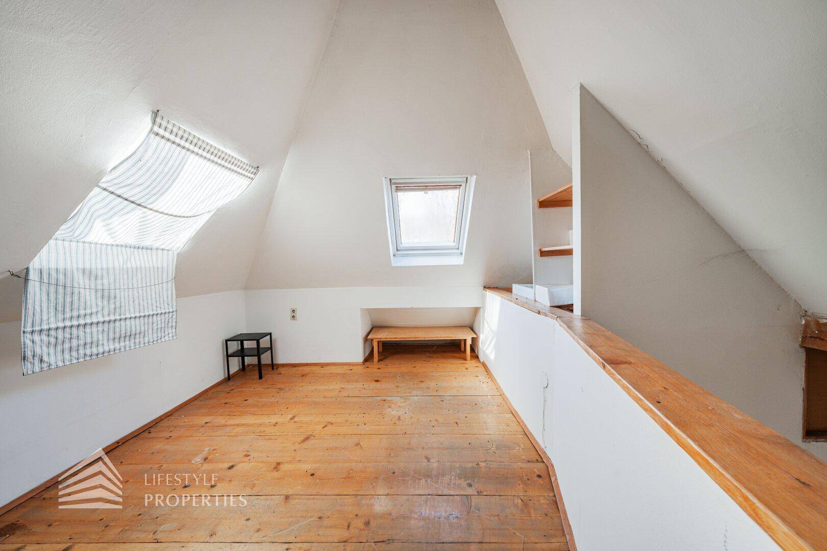 Blick von oben auf den offenen Wohnbereich im Dachgeschoss mit Kamin und Holzdielenboden.