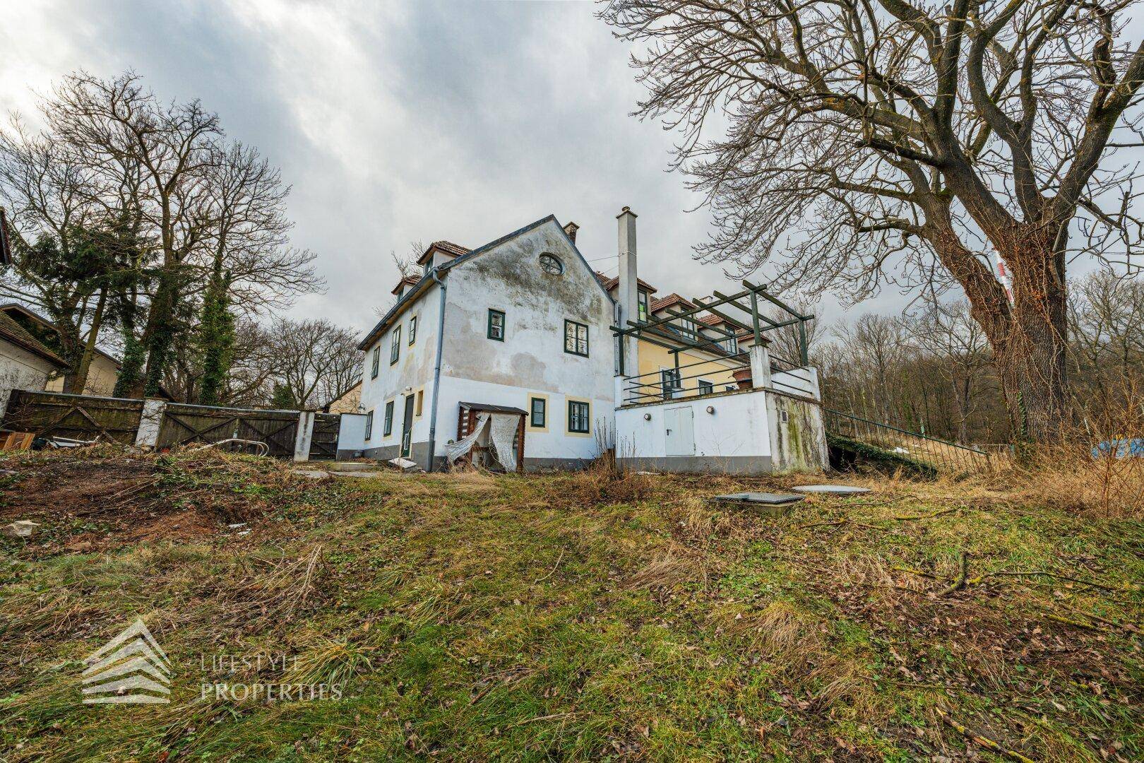 Rückansicht eines historischen Gebäudes mit weißer Fassade und einer erhöhten Terrasse.