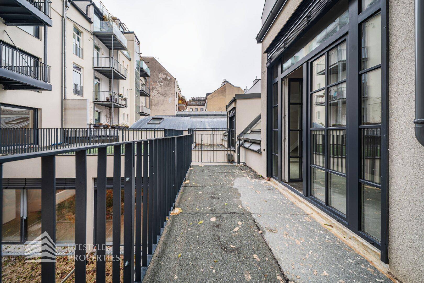 Balkon im Rohbau mit Metallgeländer und Blick auf die umliegenden Wohngebäude.
