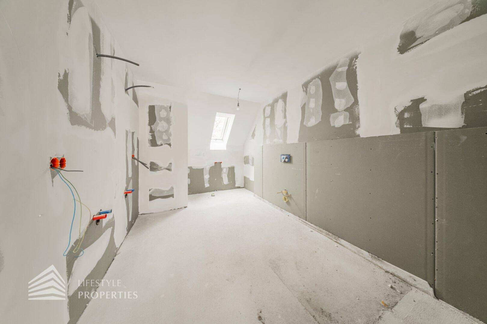 Innenraum im Rohbau mit Dachfenster und vorbereiteten Installationen für ein Badezimmer.