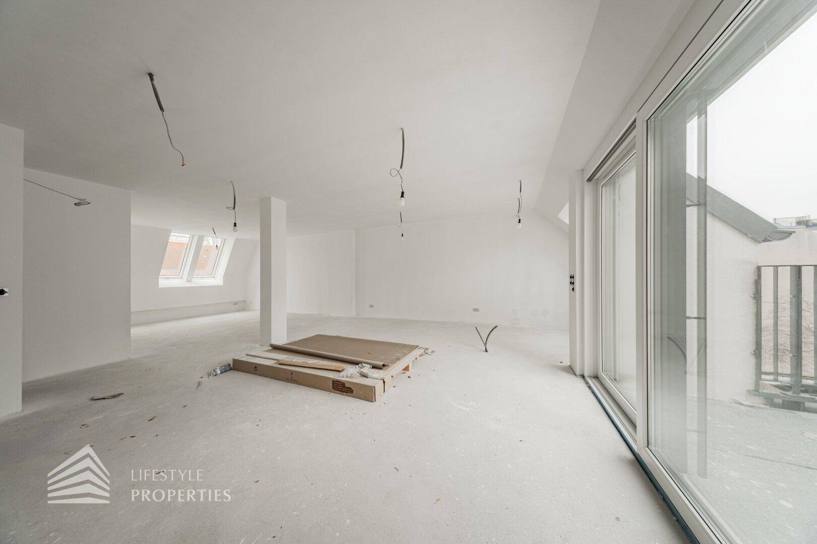 Heller, offener Wohnbereich im Rohbau mit großen Fenstern und Dachschrägen.
