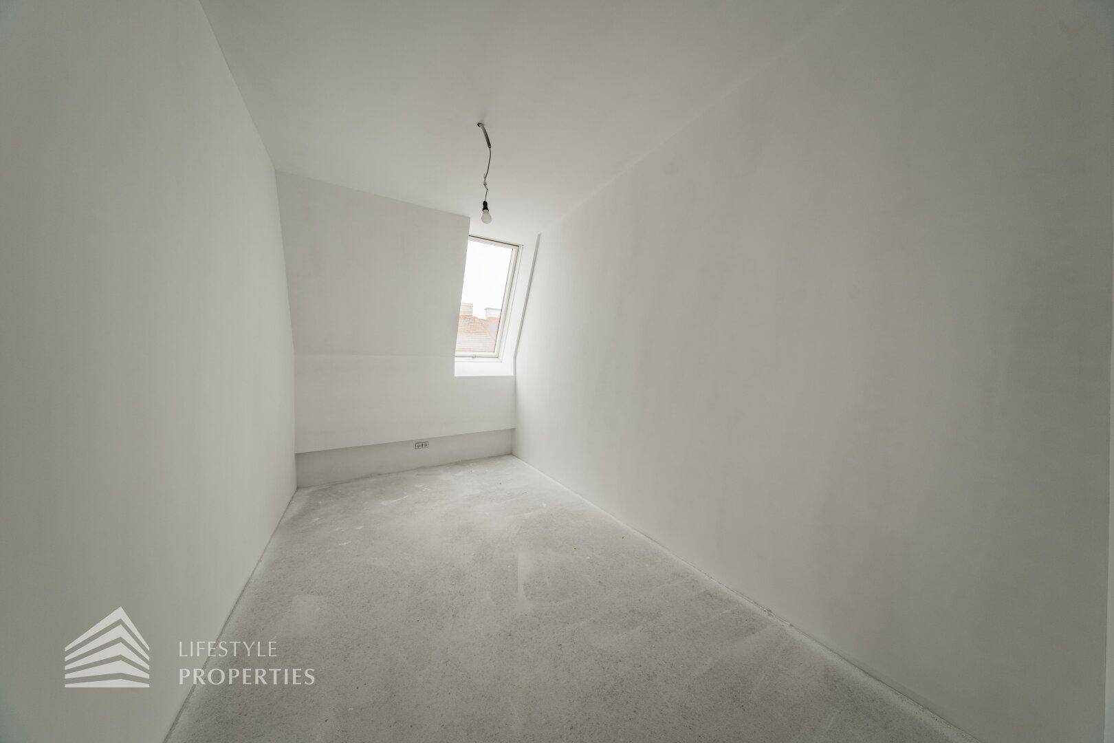 Kleinerer Raum im Rohbau mit Dachschräge und einem einzelnen Dachfenster.