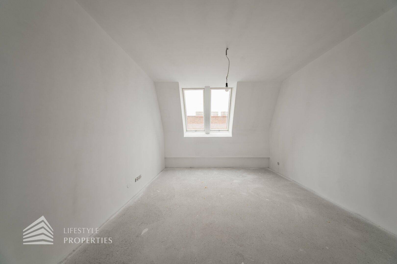 Geräumiger Raum im Rohbau mit Dachschräge und zwei nebeneinander liegenden Dachfenstern.