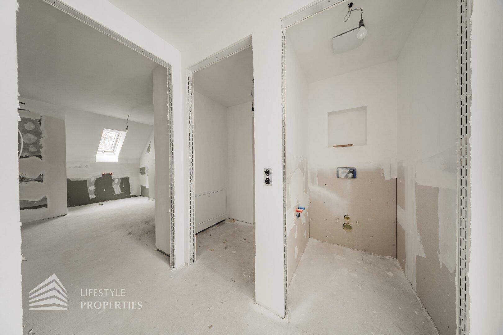 Flurbereich im Rohbau mit mehreren Türöffnungen und vorbereiteten Anschlüssen.
