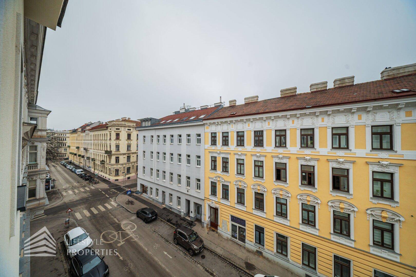 Blick von oben auf eine belebte Stadtstraße mit historischen Gebäuden und parkenden Autos.