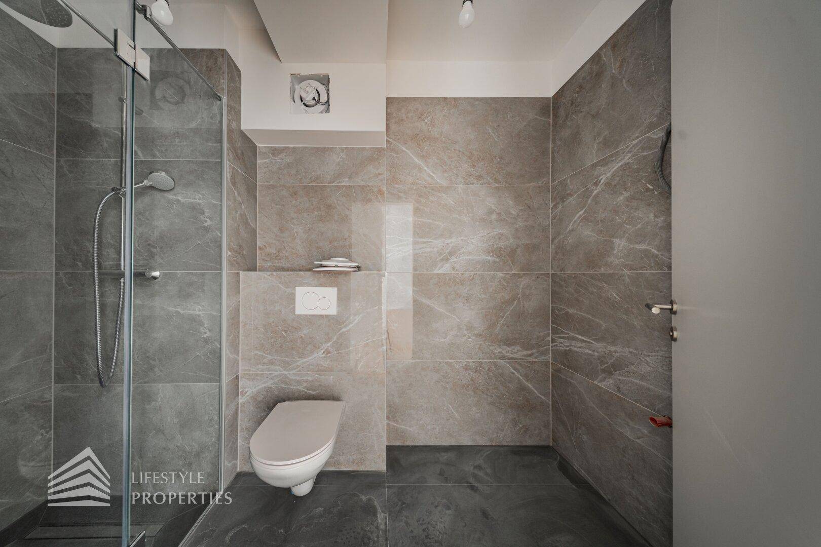 Modernes Badezimmer mit grauen Fliesen, ebenerdiger Dusche und wandhängendem WC.