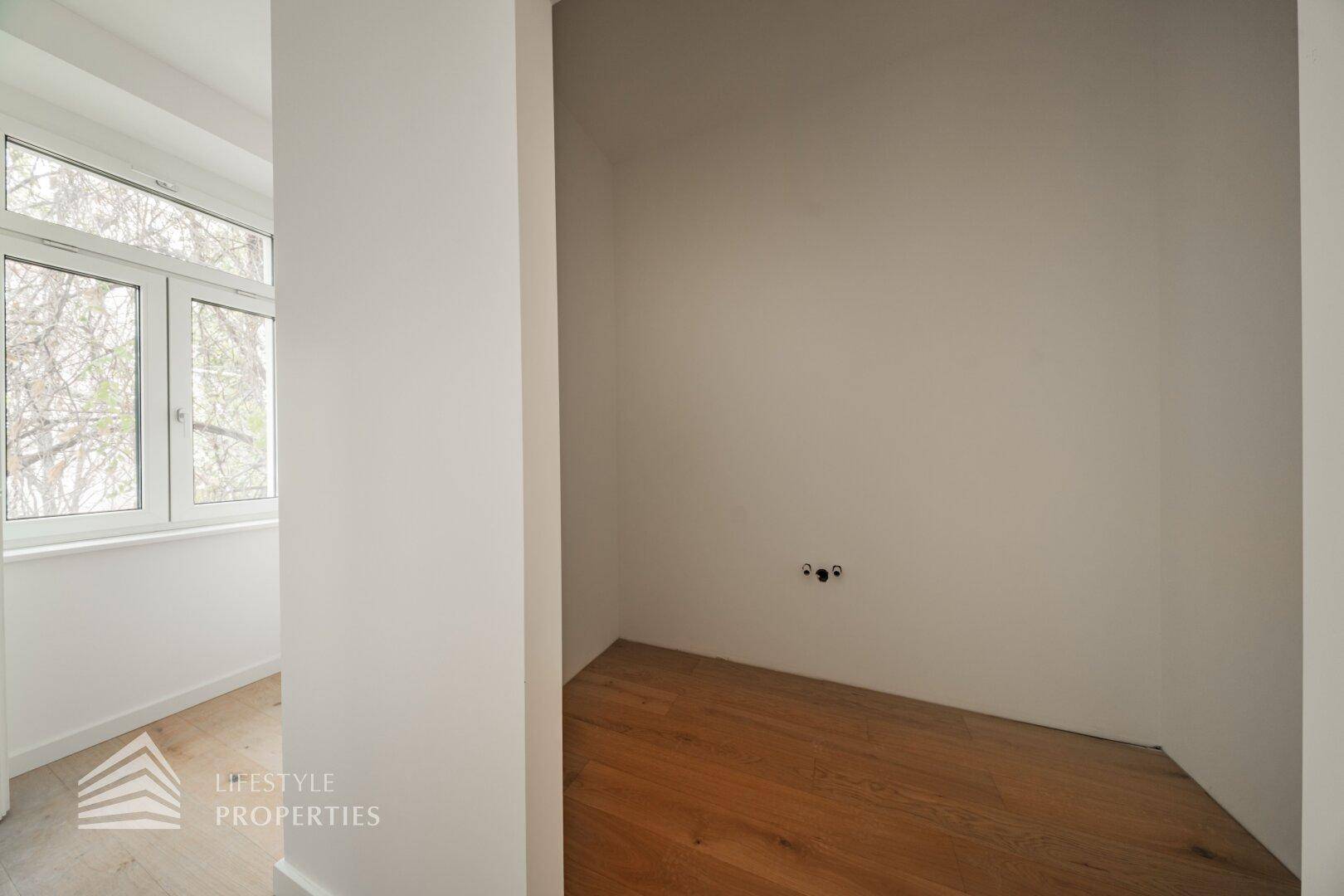Praktischer Abstellraum mit Holzboden und Anschlüssen für eine Waschmaschine neben dem Fenster.