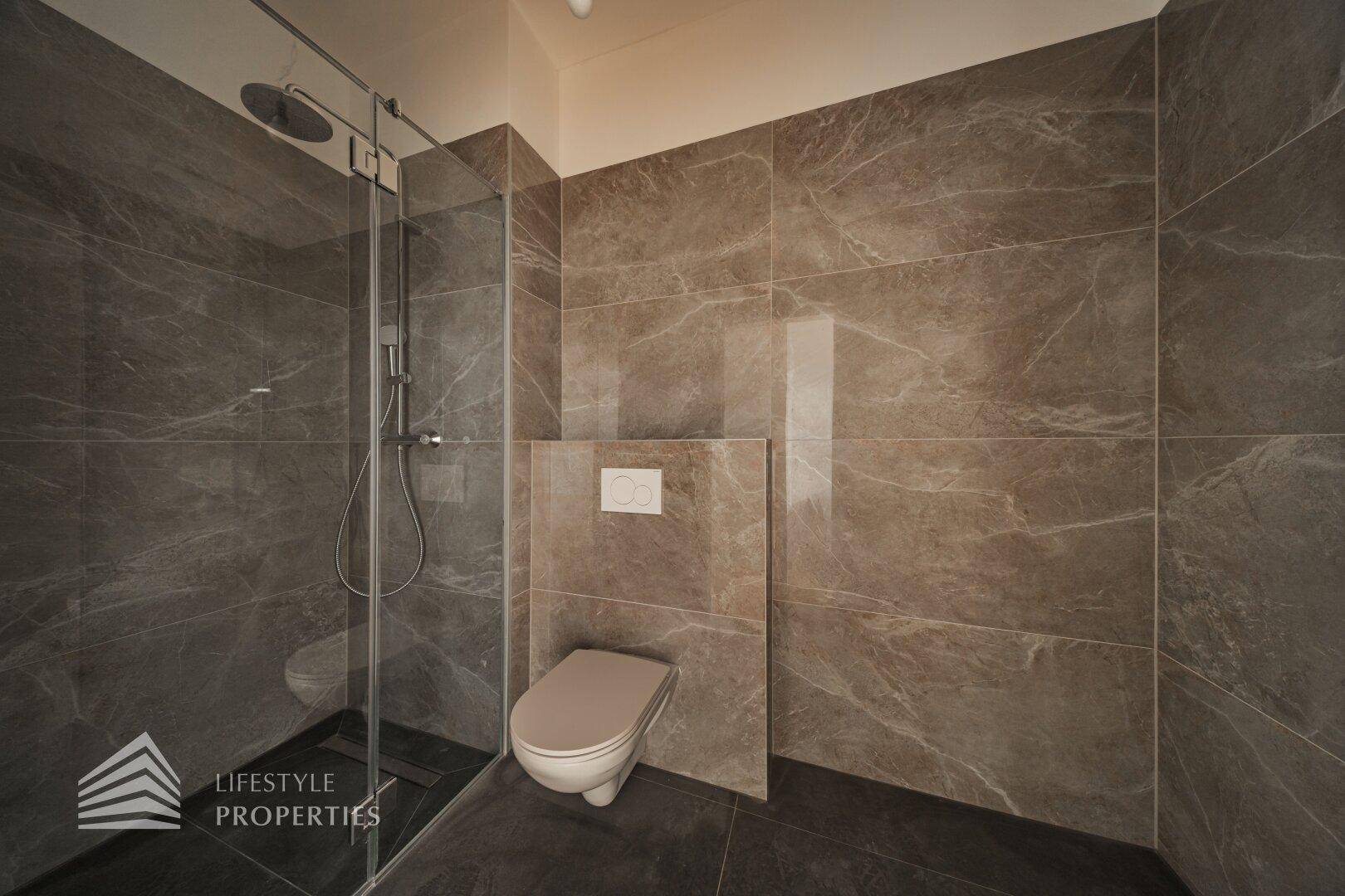 Modernes Badezimmer mit großformatigen grauen Fliesen, begehbarer Dusche und Wand-WC.