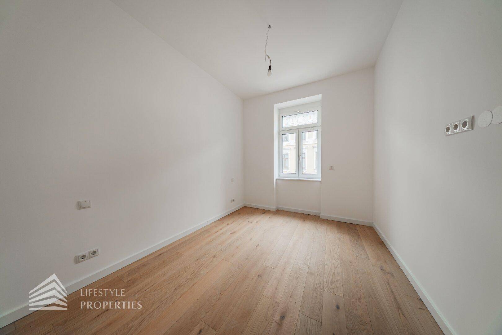 Ruhiges, helles Zimmer mit Holzboden und einem Fenster, ideal als Schlaf- oder Arbeitszimmer.