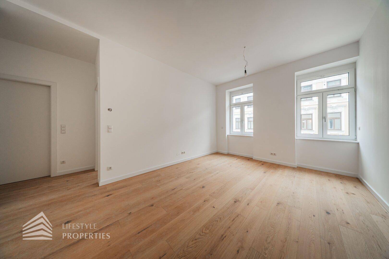Geräumiges, helles Zimmer mit Holzboden und zwei Fenstern, bietet vielseitige Nutzungsmöglichkeiten.
