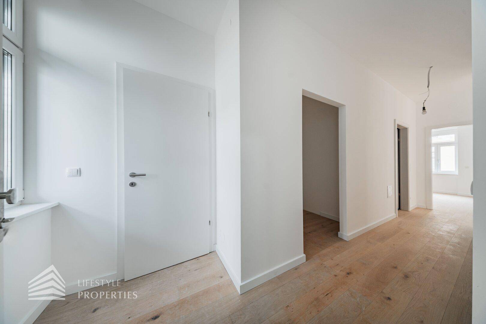 Heller Flur mit Holzboden und weißen Wänden, der zu verschiedenen Räumen führt.