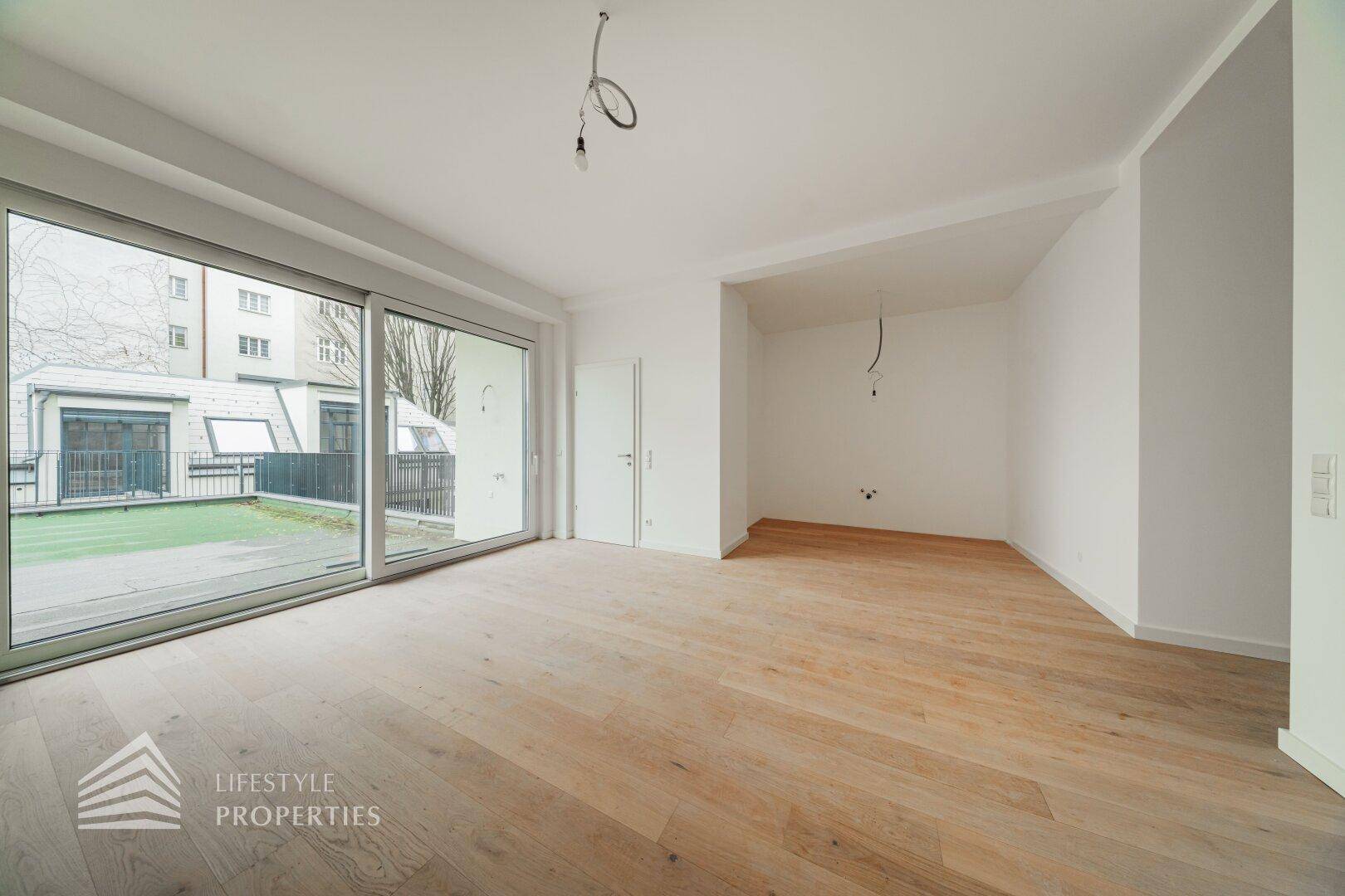 Geräumiges, helles Zimmer mit Parkettboden und Zugang zu einem Außenbereich durch eine breite Glasfront.