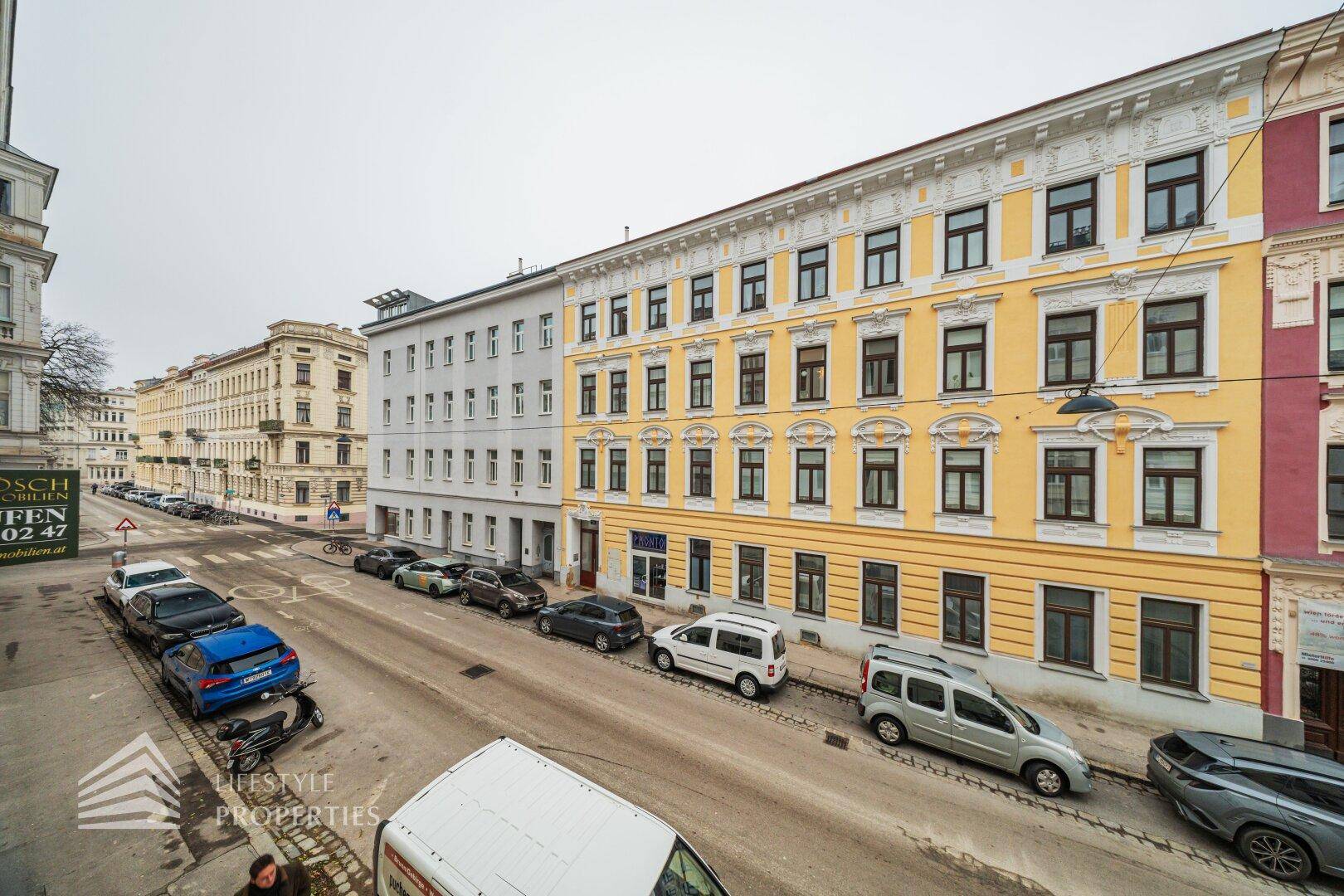 Panoramablick auf eine städtische Straße mit einer Reihe von Gebäuden und geparkten Fahrzeugen.