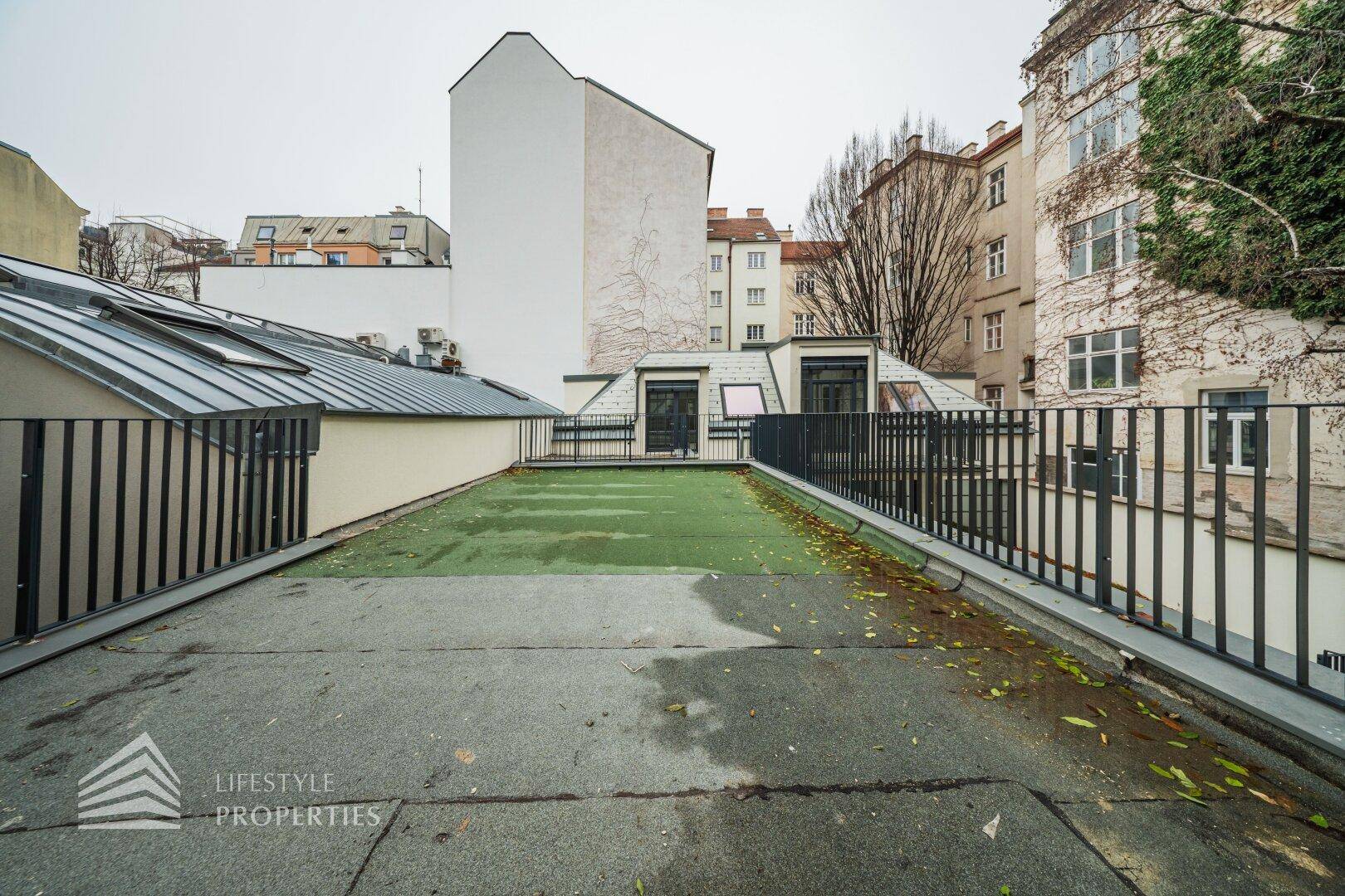 Große Dachterrasse oder Innenhof mit Kunstrasen und Blick auf umliegende Gebäude.