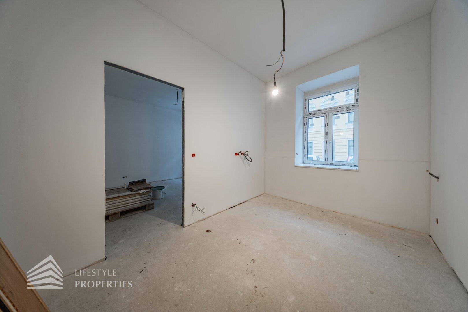 Leerer Raum im Rohbauzustand mit weiß gestrichenen Wänden und einem Fenster.