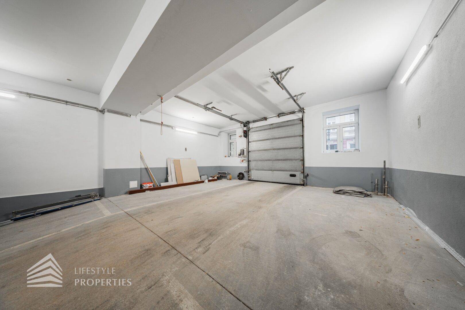 Große Garage mit Rolltor und Fenstern, bietet viel Platz für Fahrzeuge und Lagerung.