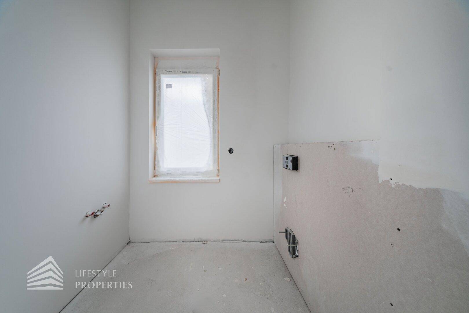 Kleiner Raum im Rohbau mit Fenster und vorbereiteten Anschlüssen für Installationen.