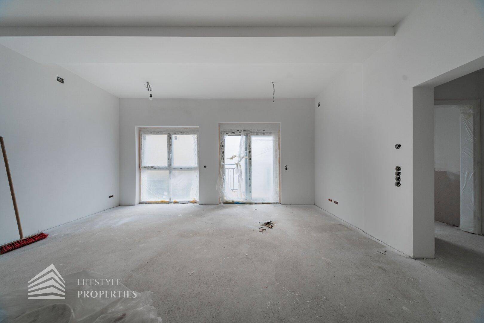 Leerer Innenraum im Bau mit abgedeckten Fenstern und Betonboden, wartet auf Fertigstellung.