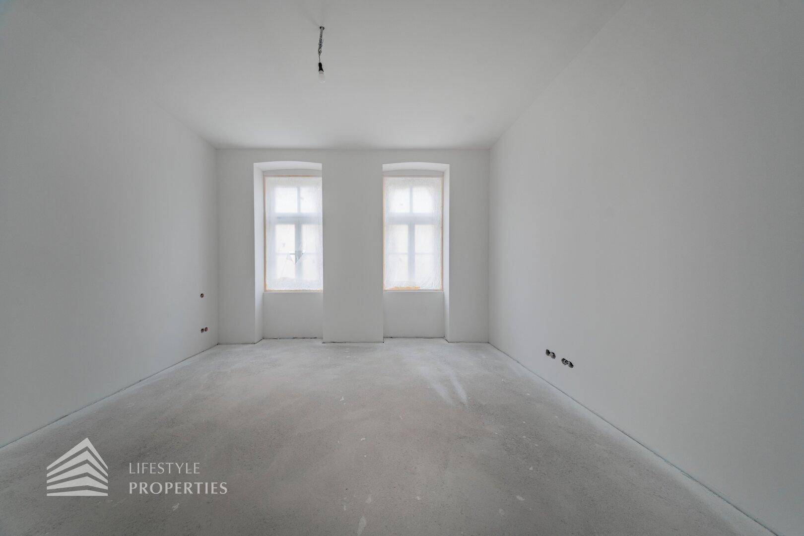 Unfertiger Raum mit zwei Fenstern und glattem Betonboden, wartet auf die Endbearbeitung.