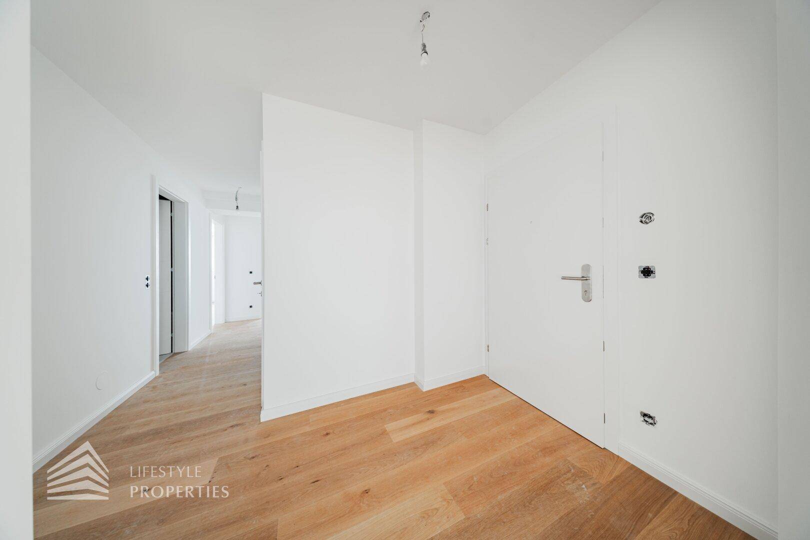 Heller Eingangsbereich mit Holzboden und weißer Tür, der zu weiteren Räumen der Wohnung führt.