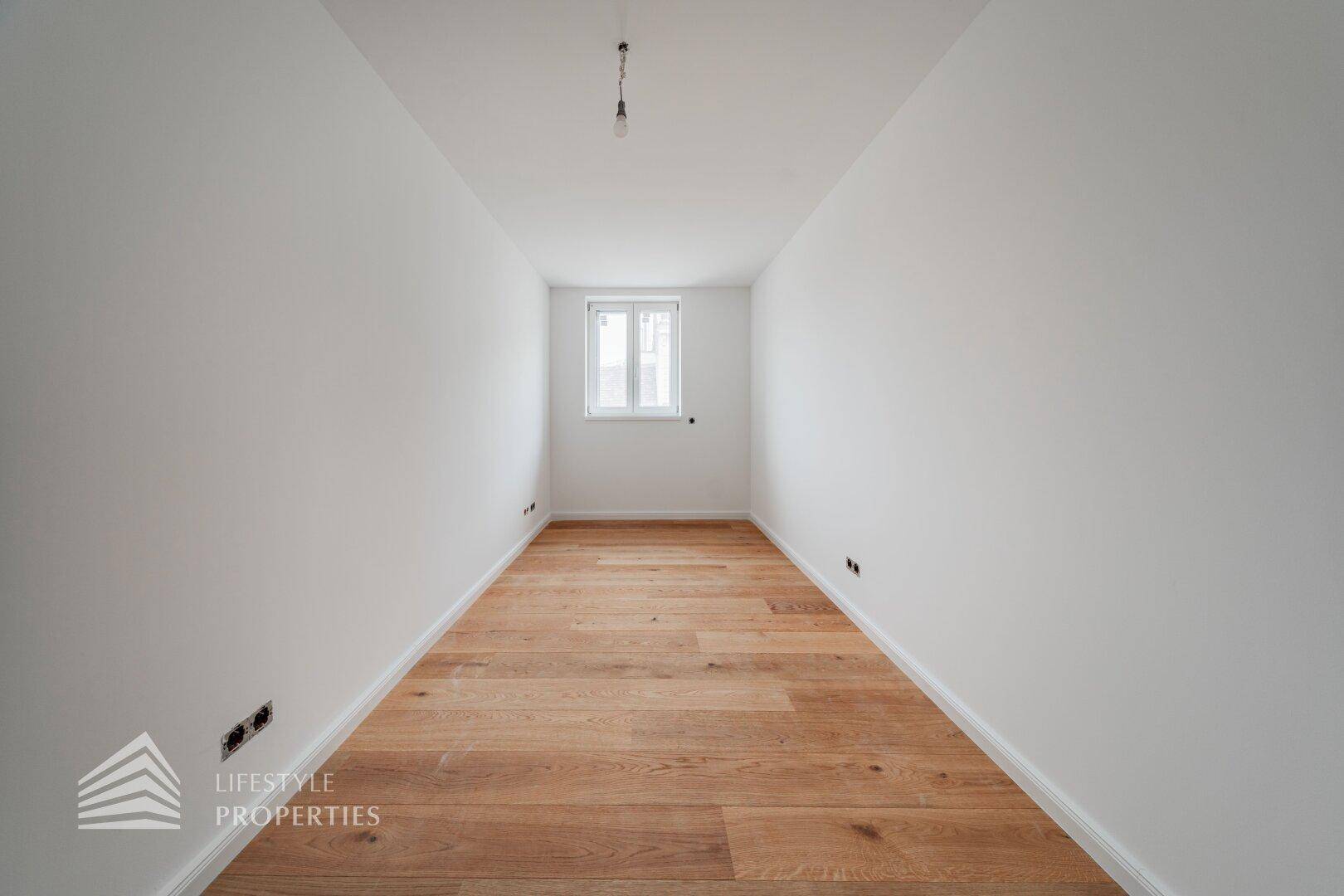 Schmaler, heller Raum mit Holzboden und Fenster, geeignet als kleines Büro oder Ankleidezimmer.