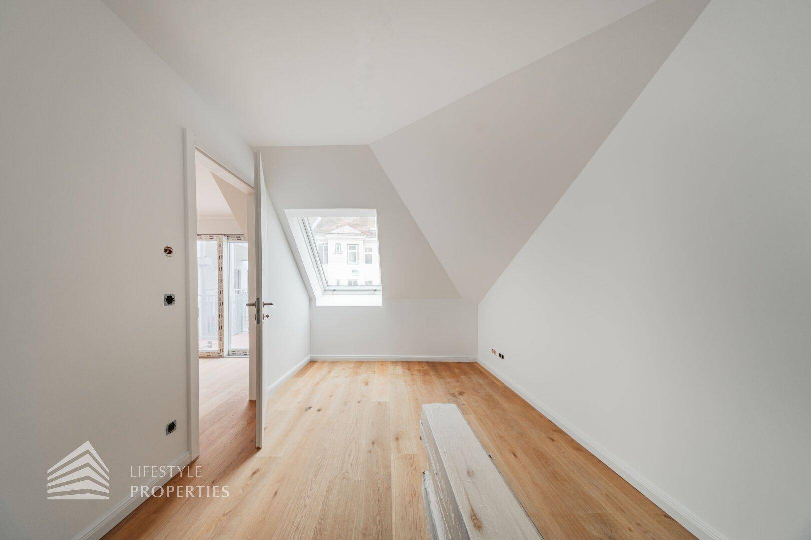 Unmöblierter Raum im Dachgeschoss mit Holzboden und Dachfenster, ideal für ein Schlafzimmer oder Büro.