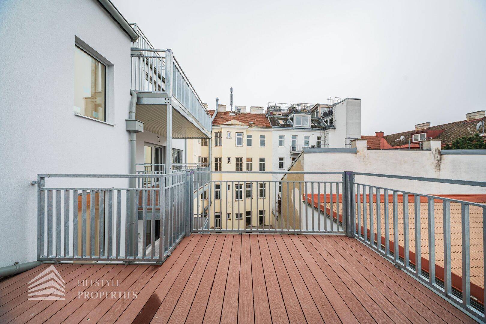 Blick von einem Balkon mit Holzboden auf die umliegenden Gebäude und weitere Balkone der Wohnanlage.