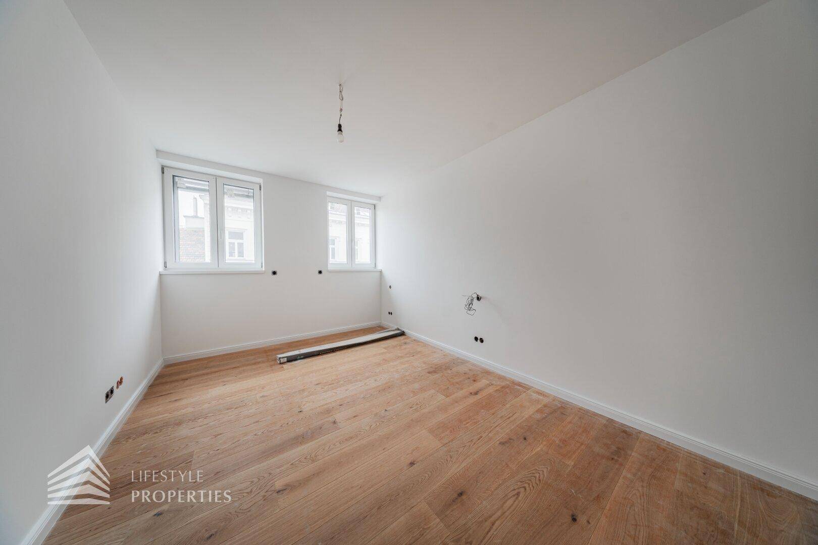Heller, unmöblierter Raum mit Holzboden und zwei Fenstern, ideal für ein Kinderzimmer oder Arbeitszimmer.