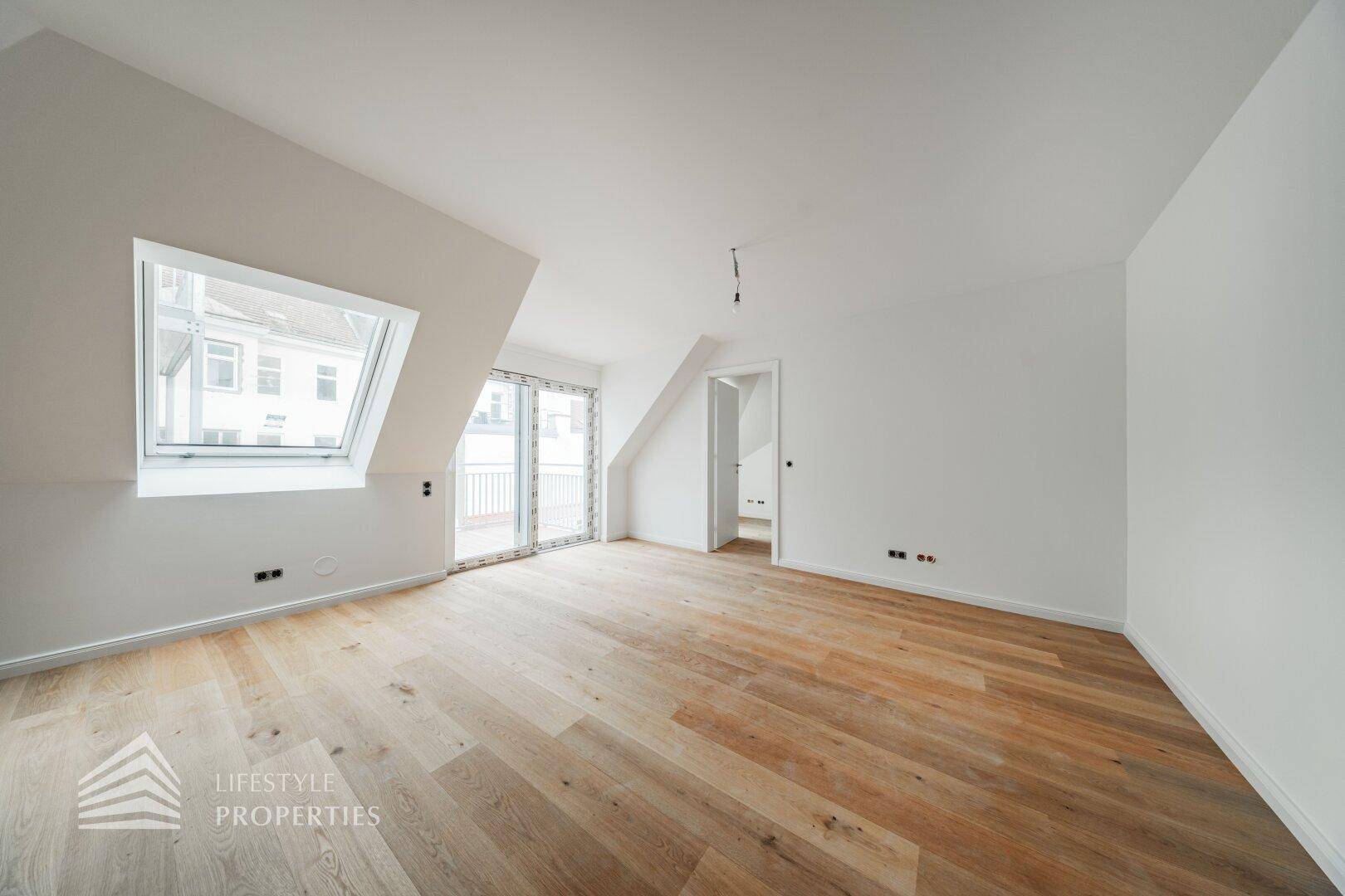 Lichtdurchfluteter Raum im Dachgeschoss mit Holzboden, Dachfenster und Zugang zu einem Balkon.
