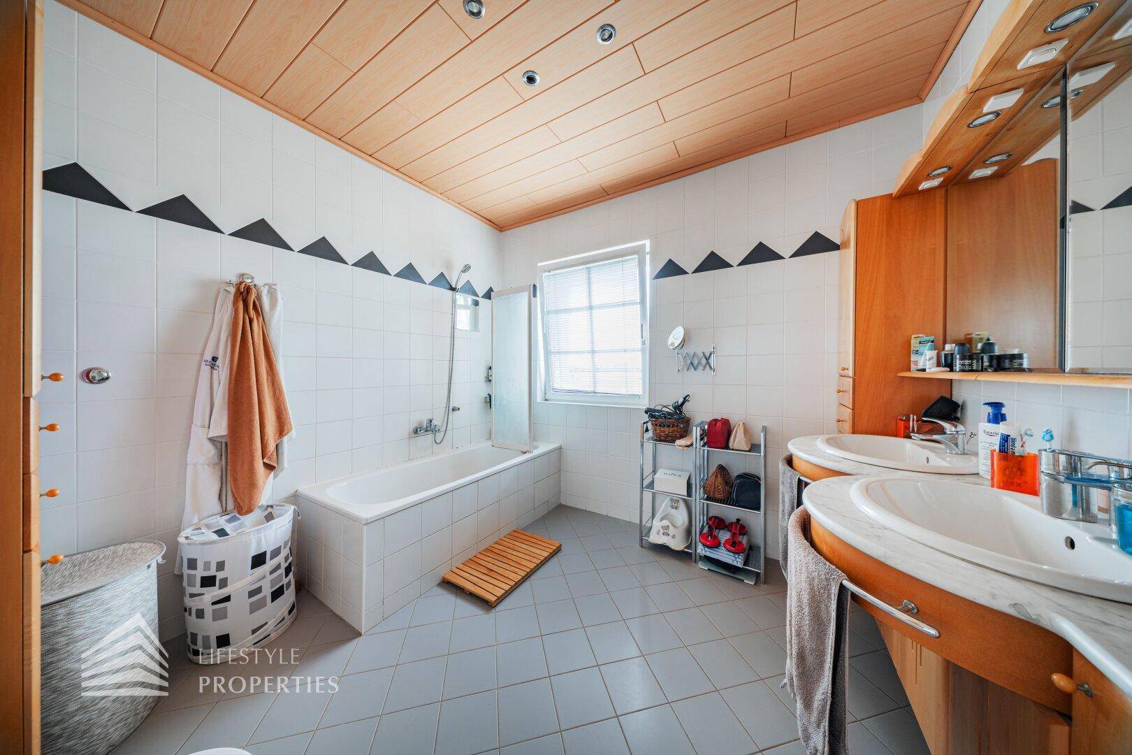 Geräumiges Badezimmer mit Doppelwaschbecken, Badewanne und Holzdecke für eine warme Atmosphäre.
