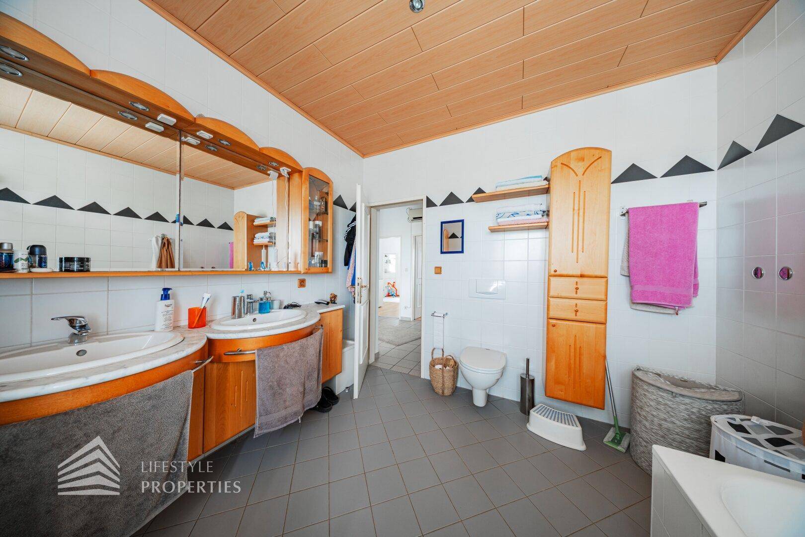 Großes Badezimmer mit Doppelwaschbecken, Badewanne, WC und Holzdecke.