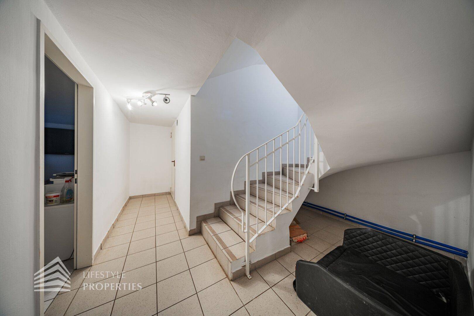 Treppenabgang in den Keller mit Fliesenboden und Zugang zu verschiedenen Kellerräumen.