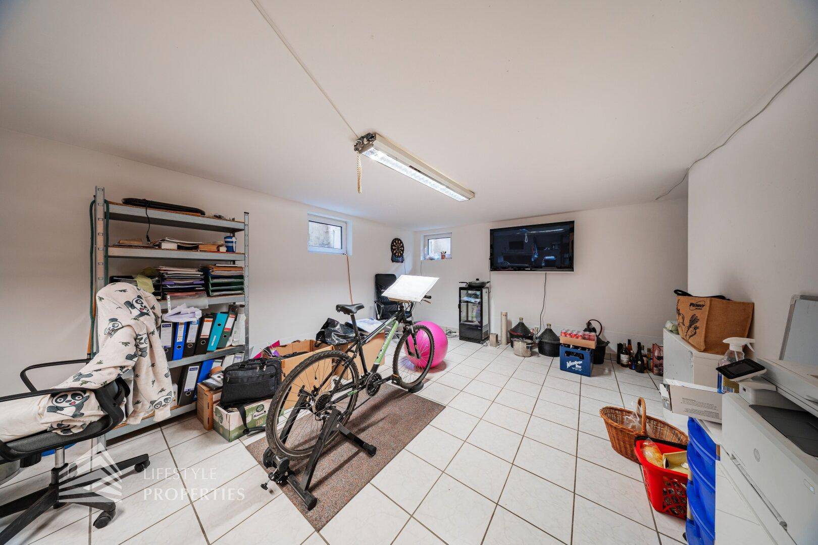 Geräumiger Kellerraum mit Fliesenboden, Fernseher und vielseitigen Nutzungsmöglichkeiten als Hobbyraum.