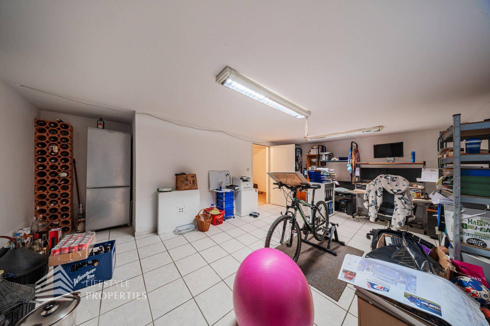 Vielseitiger Kellerraum mit Fliesenboden, Fahrradtrainer und Stauraum für Hobbys und Freizeit.