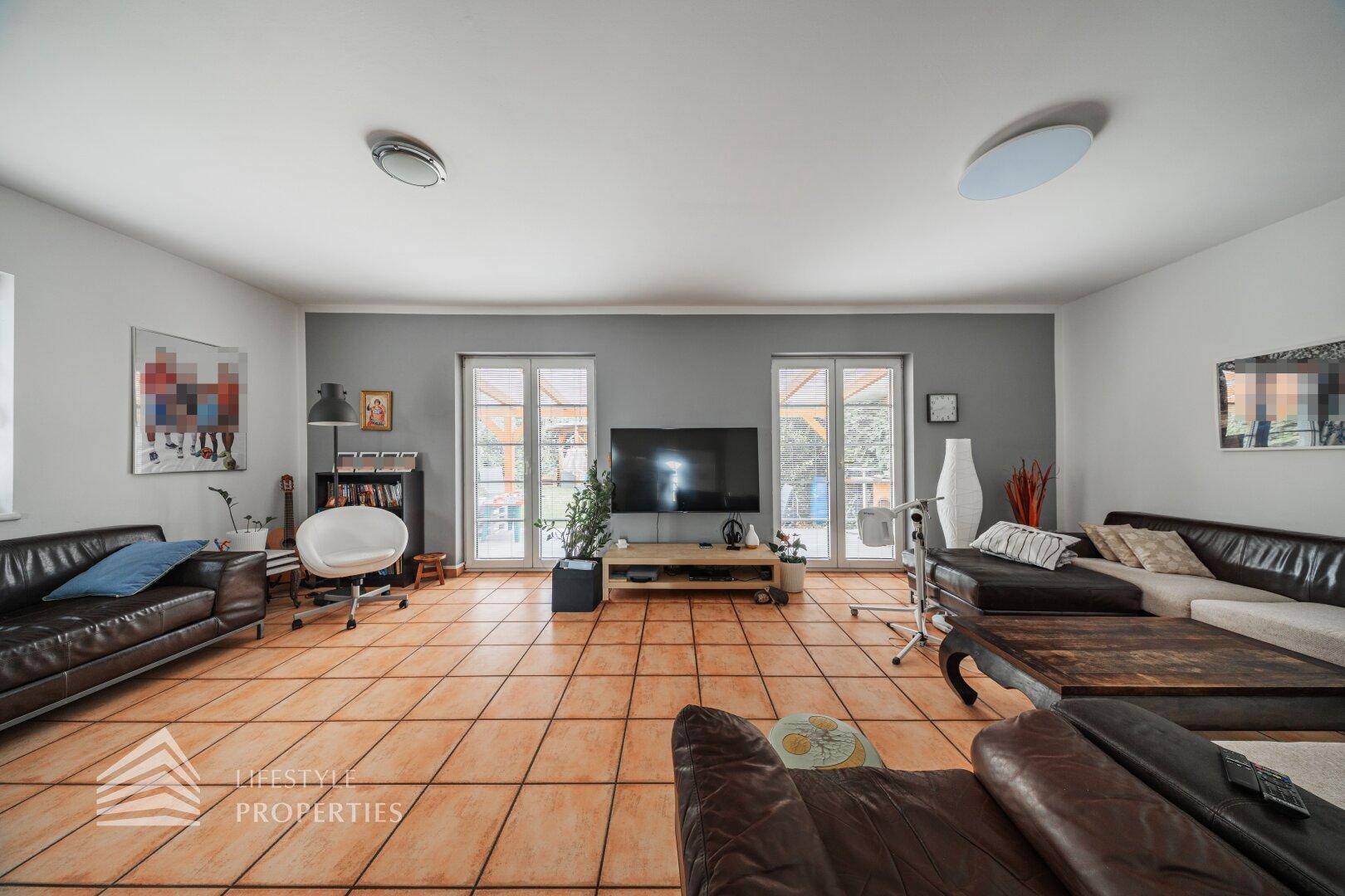 Großzügiges Wohnzimmer mit Terracotta-Fliesen, bequemen Sofas und großen Fenstern zur Terrasse.
