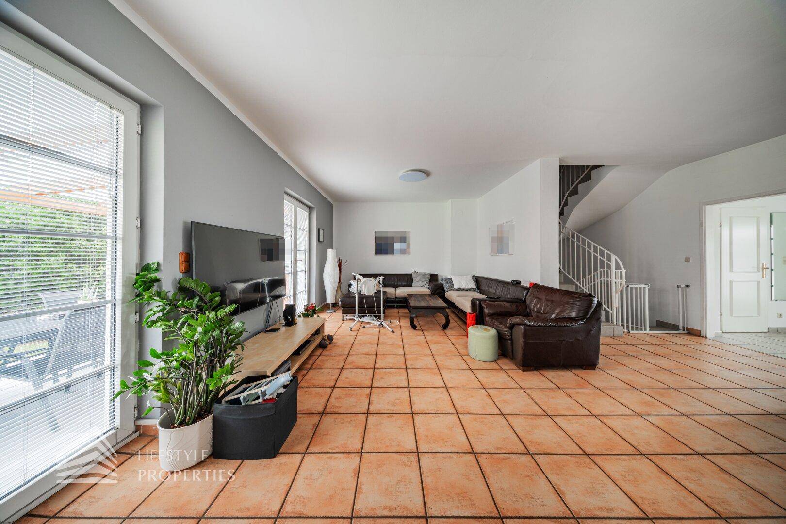 Lichtdurchflutetes Wohnzimmer mit Terracotta-Fliesen und direktem Zugang zur überdachten Terrasse.