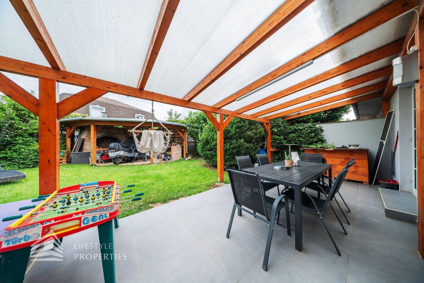 Geräumige überdachte Terrasse mit Esstisch und Blick auf den Garten mit Spielmöglichkeiten.