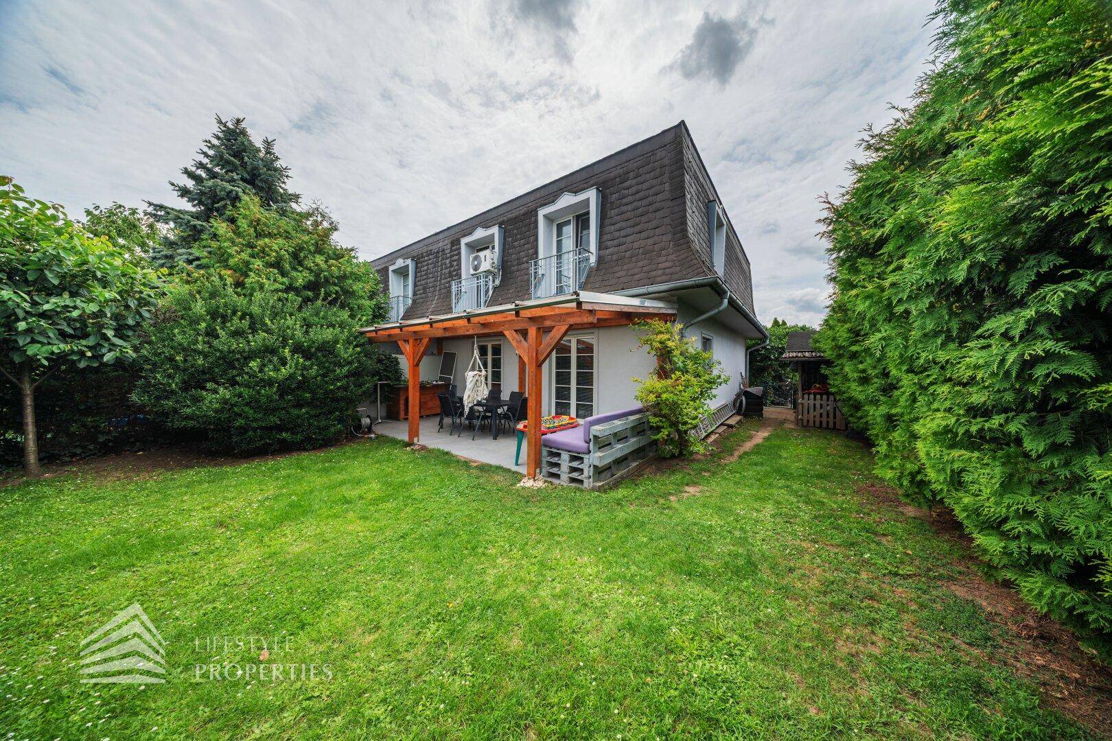 Weitläufiger Gartenbereich hinter dem Haus mit überdachter Terrasse und üppiger Bepflanzung.