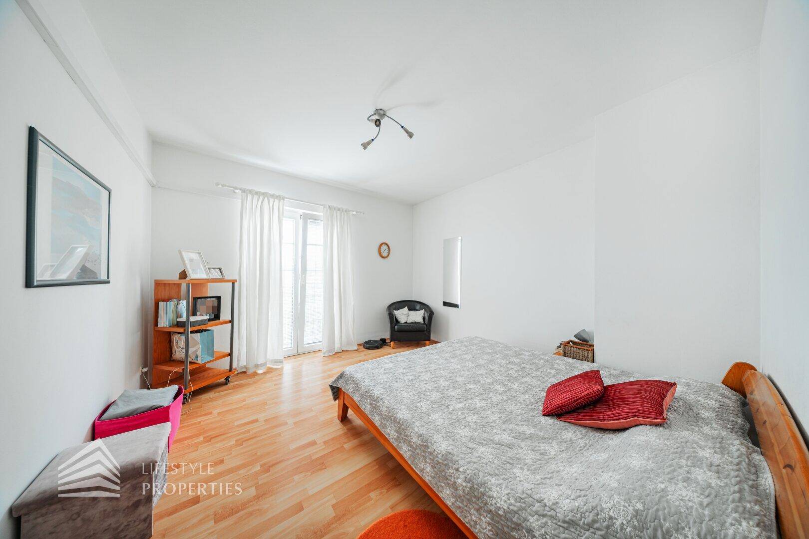 Helles Schlafzimmer mit Parkettboden, Doppelbett und Zugang zu einem französischen Balkon.